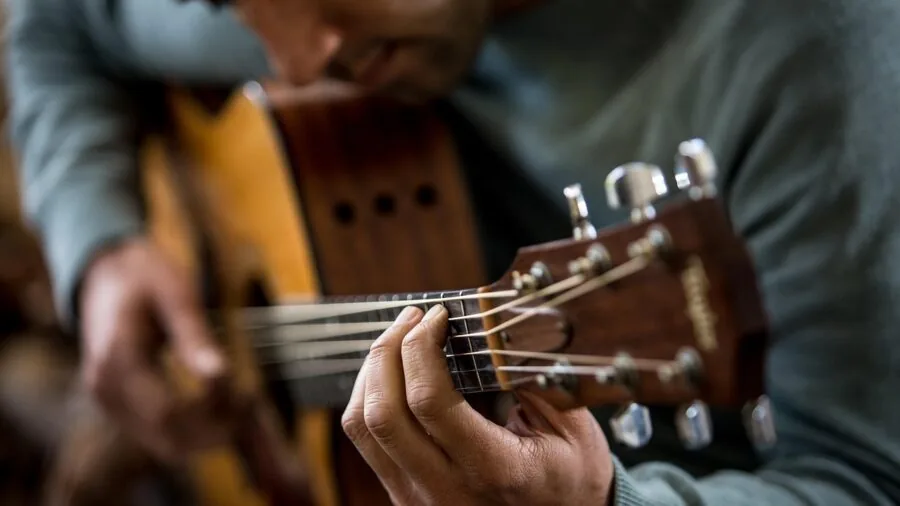 Guitarist adjusting tuning pegs on electric guitar during practice session
