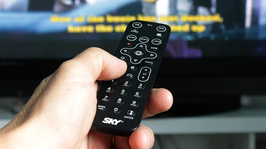Hand holding remote control pointing at modern fan device in living room