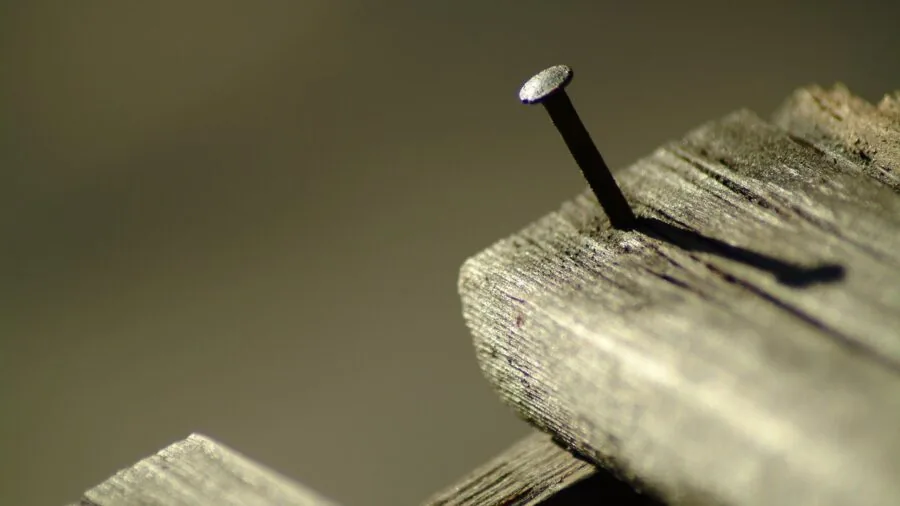 Hands carefully extracting a nail from wooden surface using a pry bar tool