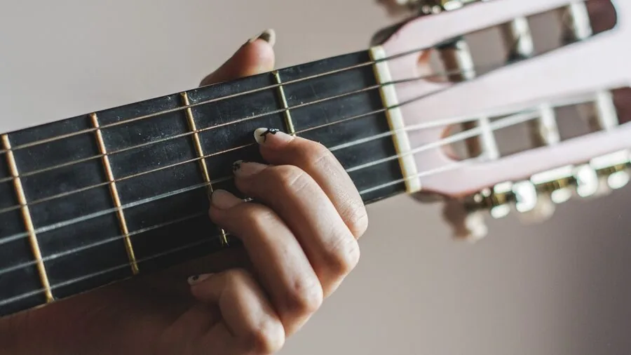 Hands positioned on classical guitar neck and strings during playing