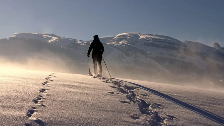 Hiker on mountain trail adjusting trekking pole length while hiking uphill through rocky terrain