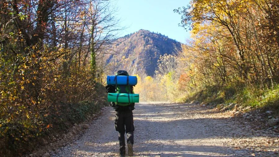 Hiker packing light gear into small backpack on mountain trail
