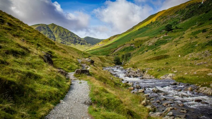 Hiker wading through stream on mountain trail during rainy weather conditions