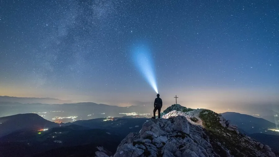 Hiker wearing headlamp on dark forest trail at night, demonstrating practical headlamp use