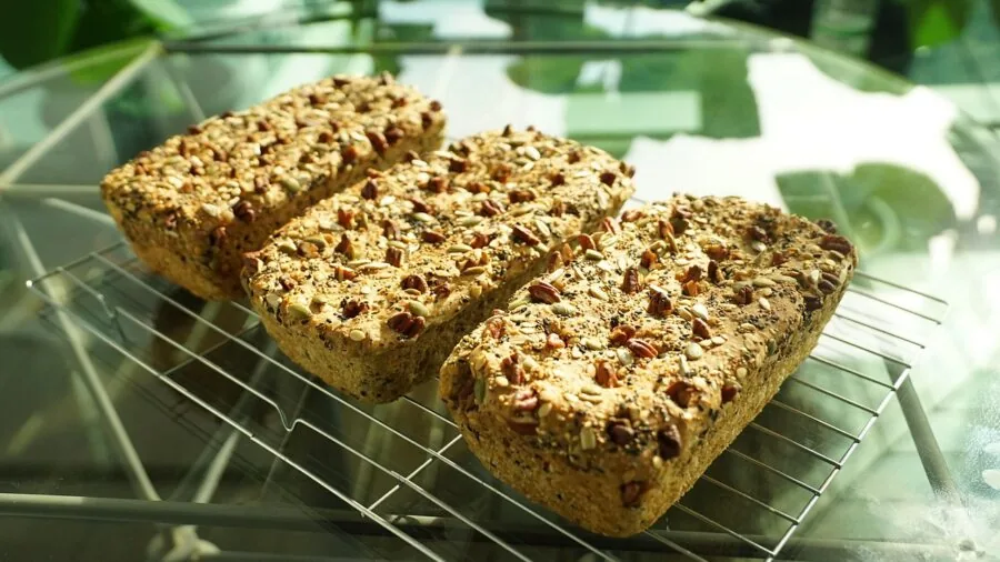 Home baker arranging freshly baked cookies on cooling rack over sheet pan in bright kitchen