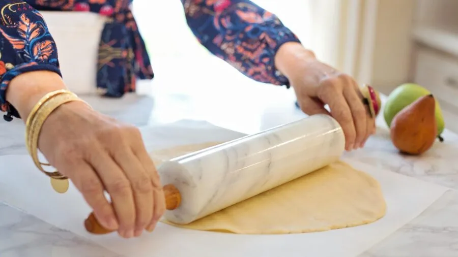 Home baker rolling out pastry dough on a large wooden work surface with flour