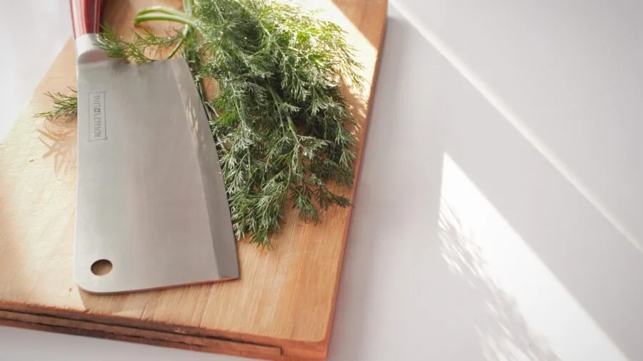 Home cook sharpening a chef knife at proper angle on cutting board in natural light kitchen setting
