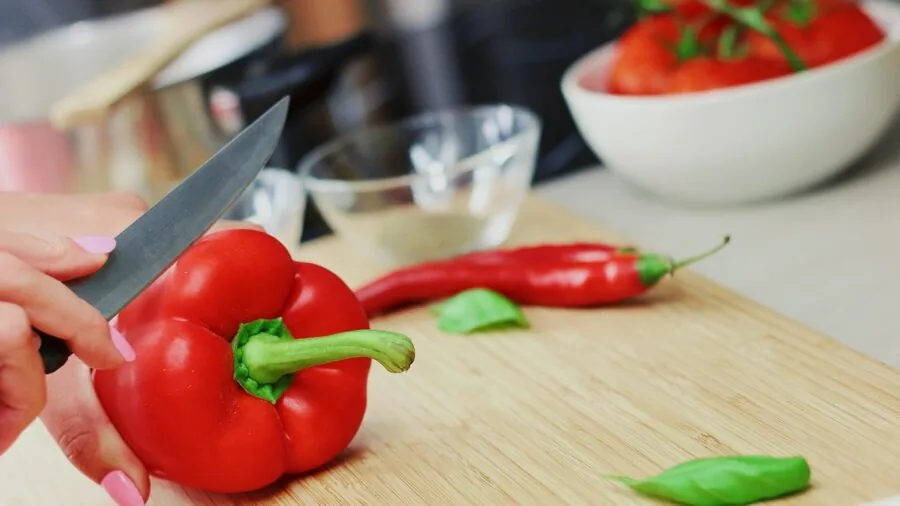 Home cook using handheld mandoline slicer over cutting board with fresh vegetables in bright kitchen