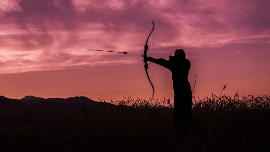 Hunter drawing compound bow while aiming at target in natural outdoor setting