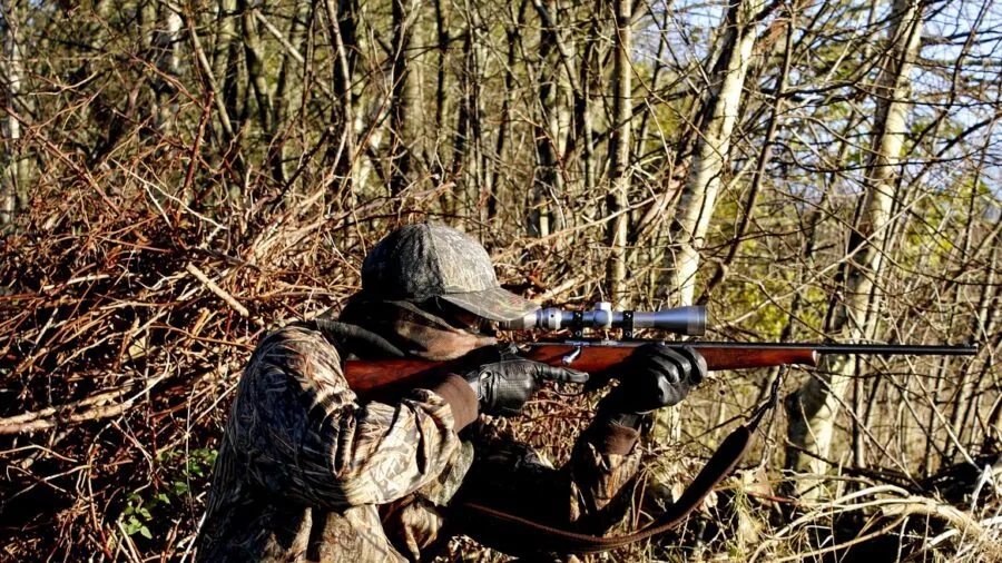 Hunter in camouflage gear gripping rifle while trekking through misty forest terrain