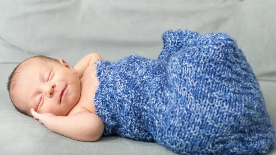 Infant sleeping peacefully during swaddle transition phase with arms positioned comfortably