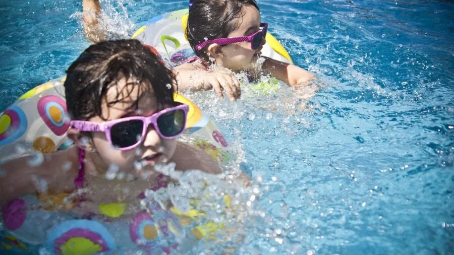 Kids enjoying colorful pool toys and floats in backyard swimming pool on sunny day