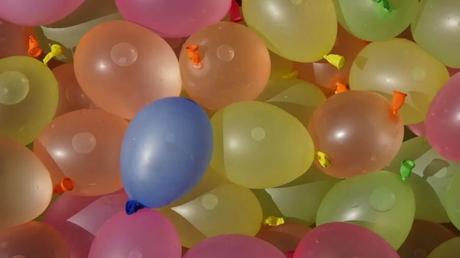 Kids laughing and running through water balloons during outdoor summer play in backyard