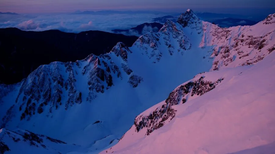 Male hiker traversing snowy mountain terrain in winter conditions wearing warm layered clothing