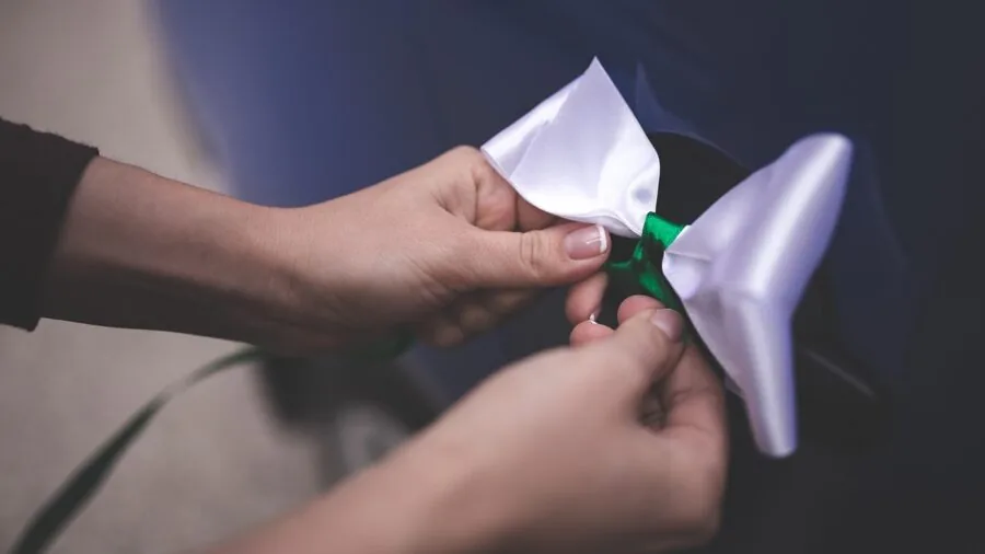 Man adjusting self-tie bow tie in mirror, getting dressed for formal event