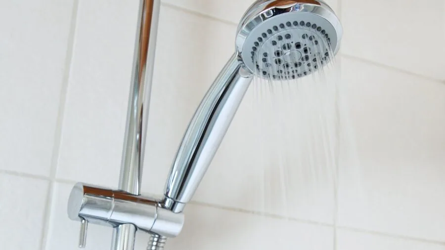 Man applying aftershave spray in modern bathroom mirror reflection during grooming routine