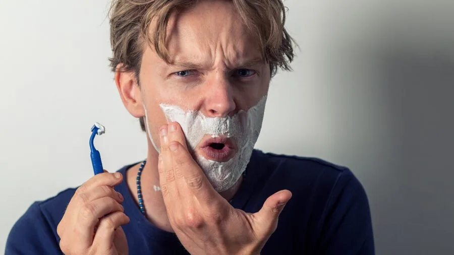 Man grooming his beard with care in bathroom mirror, showing daily beard maintenance routine