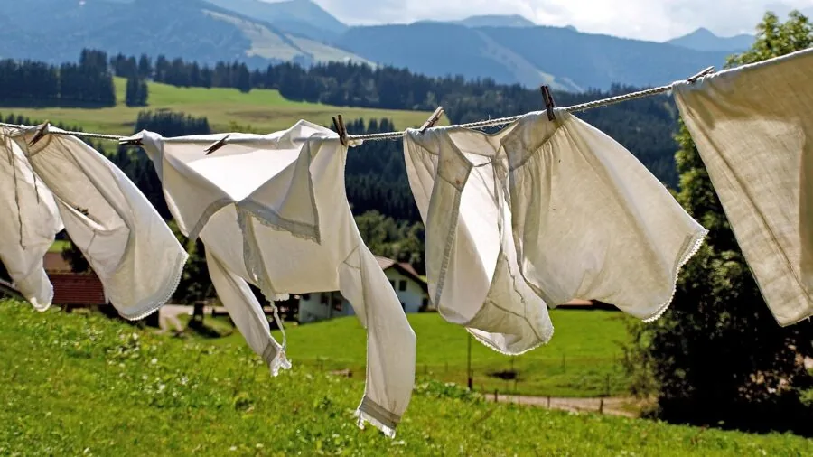 Man hanging freshly washed clothes on a clothesline to air dry outdoors in natural sunlight