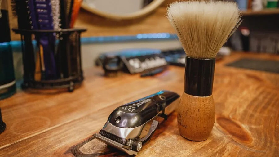 Man holding beard brush while grooming facial hair in bathroom mirror, demonstrating proper brushing technique