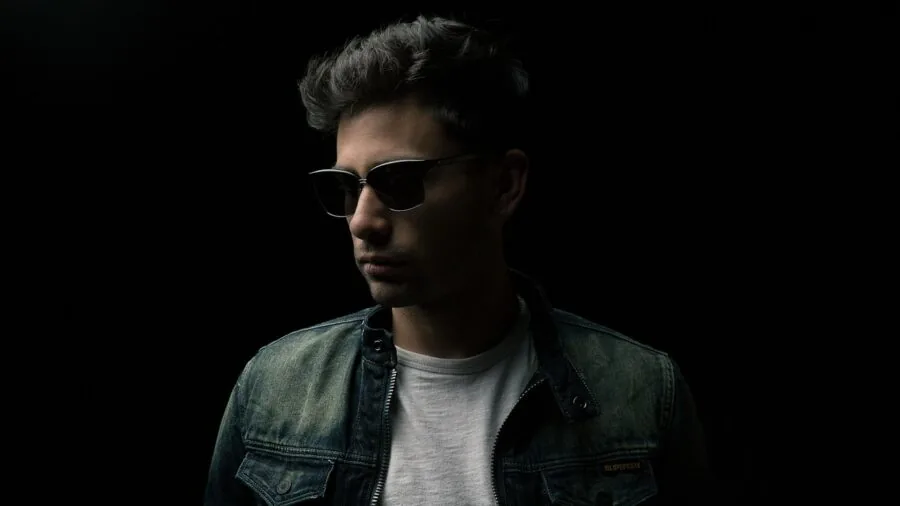 Man in denim jacket layered over light shirt in natural outdoor setting