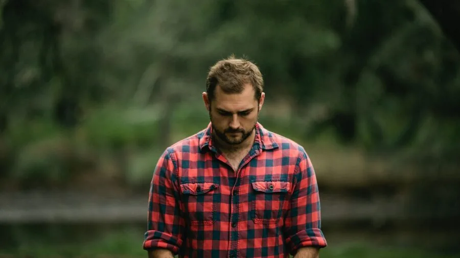 Man in flannel shirt working outdoors, demonstrating durability and quality construction in natural light