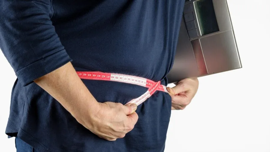 Man measuring his waist size with a tape measure while wearing casual clothing