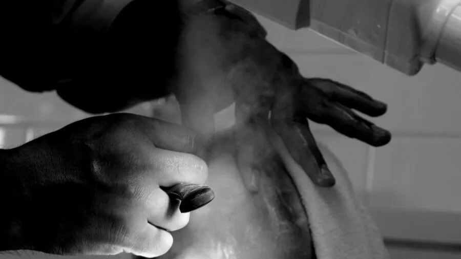 Man performing traditional wet shave with straight razor in bathroom mirror reflection