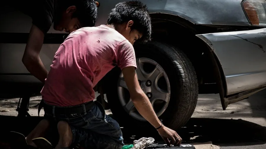 Mechanic in work clothes lying on padded creeper seat under car doing maintenance work