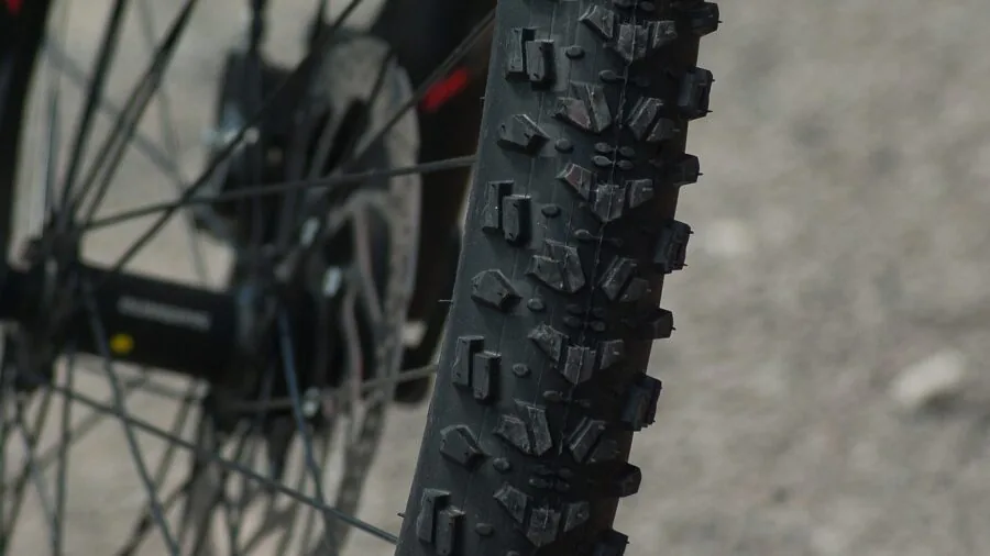 Mountain biker adjusting tubeless tire pressure on trail with natural landscape background