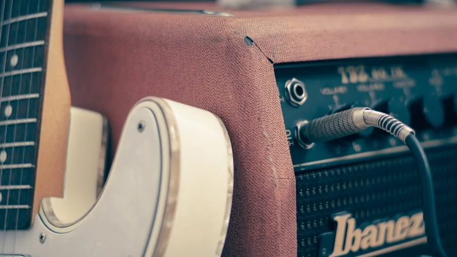 Musician adjusting guitar effects while playing through amplifier in studio setting