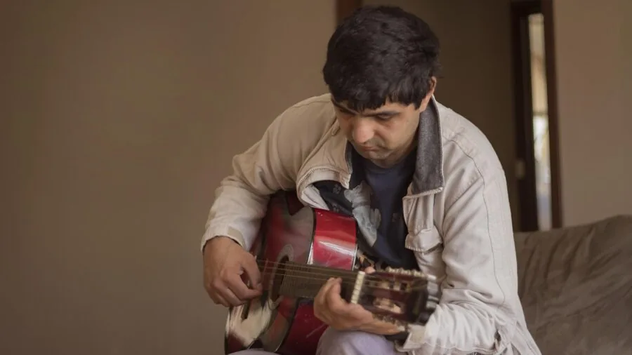 Musician adjusting guitar tuning while practicing with metronome in home studio setting