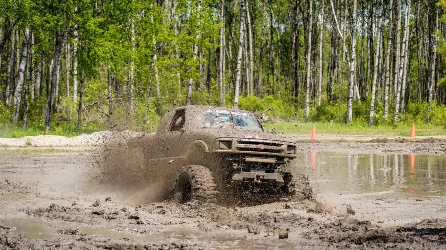 Off-road truck navigating through muddy terrain in rugged wilderness setting