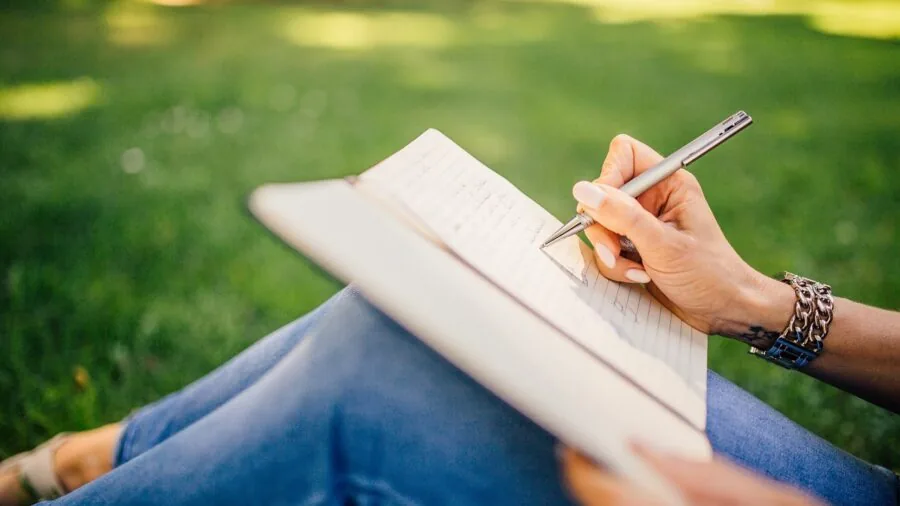 Older adult writing in notebook with pen at table, demonstrating memory reinforcement through handwriting