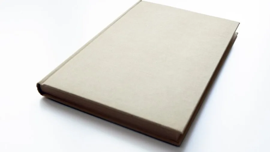 Open hardcover notebook on wooden desk with pen and coffee cup in natural lighting