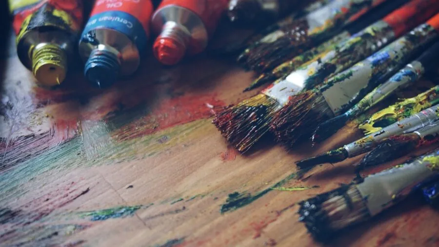 Overhead view of organized art supplies including brushes, paints, and canvas arranged on wooden table