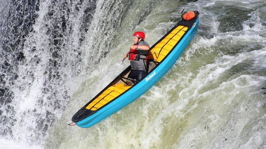 Paddler sitting in canoe on calm lake, demonstrating proper seating posture during outdoor water activity