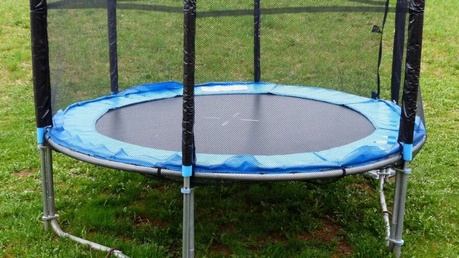 Parent and child securing trampoline net attachment straps during backyard setup installation