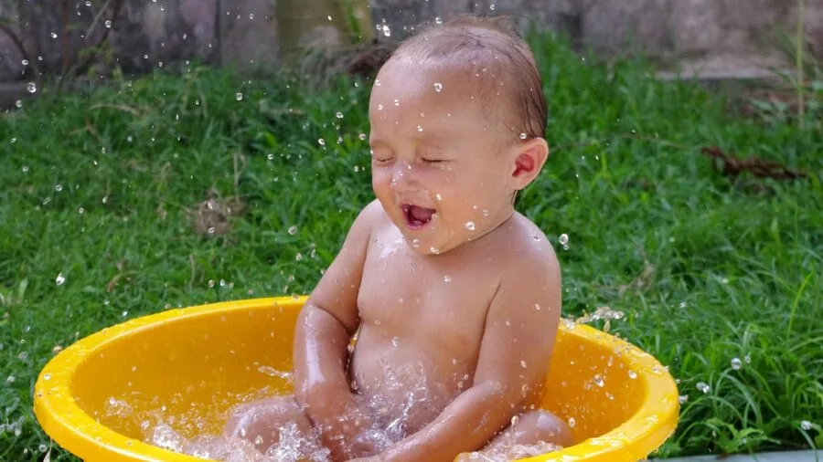 Parent carefully testing warm bathwater temperature while bathing newborn baby in bathroom