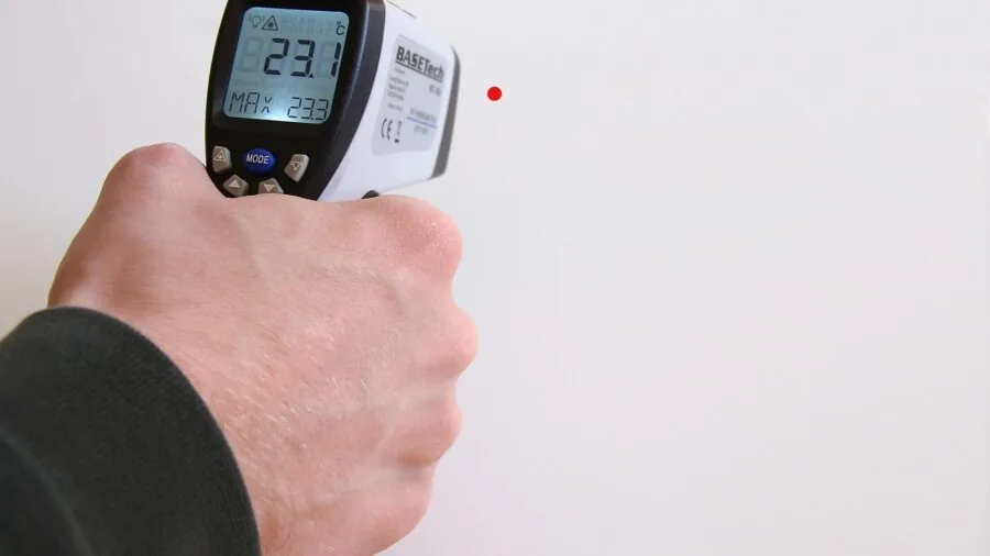 Parent checking nursery temperature with thermometer on wall near crib