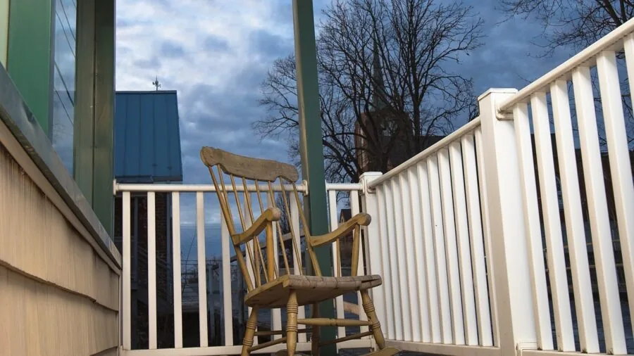 Parent gently rocking in wooden chair beside sleeping infant in soft nursery lighting