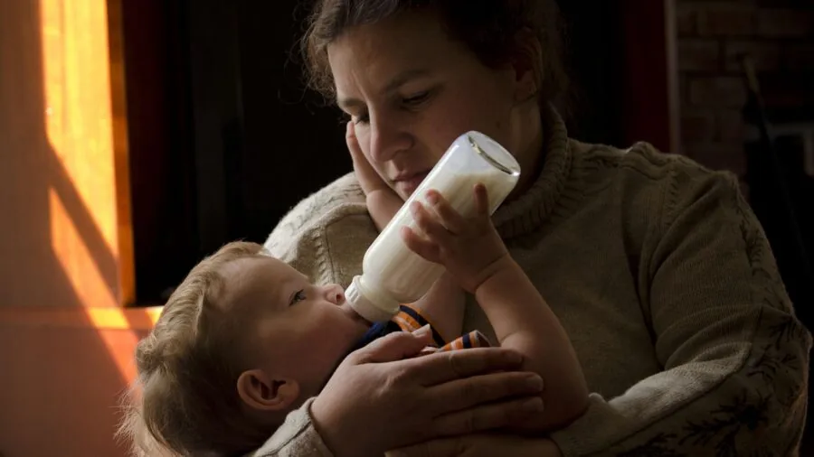 Parent holding baby bottle with concerned expression during feeding time