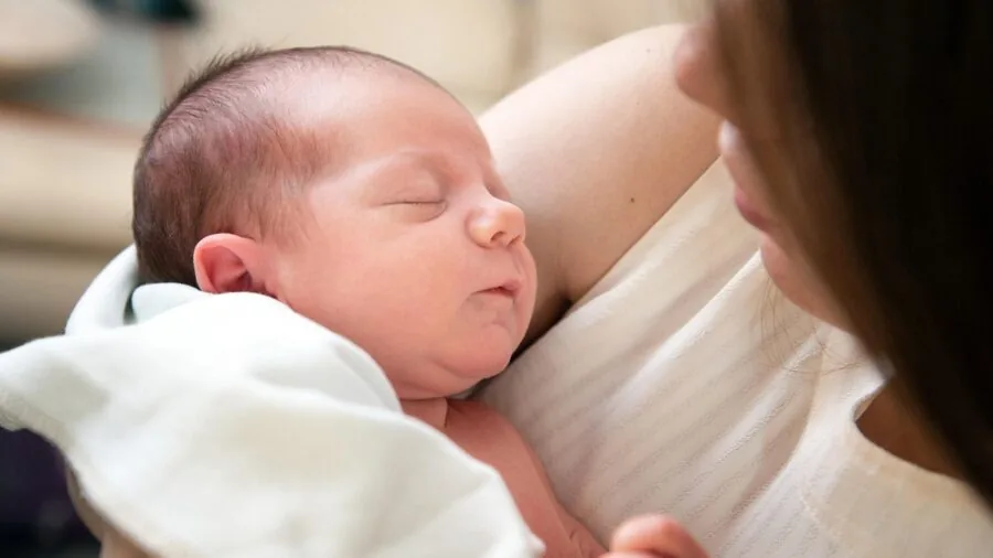 Parent leaning over crib observing peacefully sleeping infant in bright nursery room