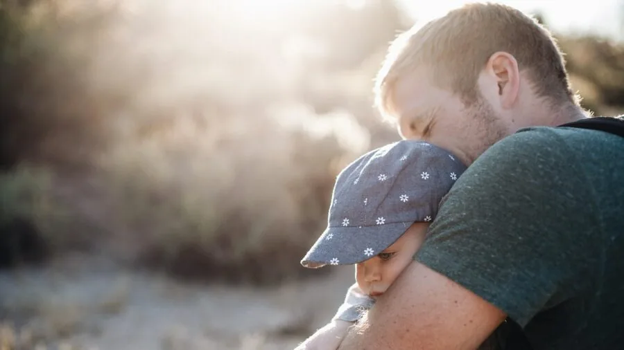 Parent looking frustrated while trying to put mittens on squirming baby's hand