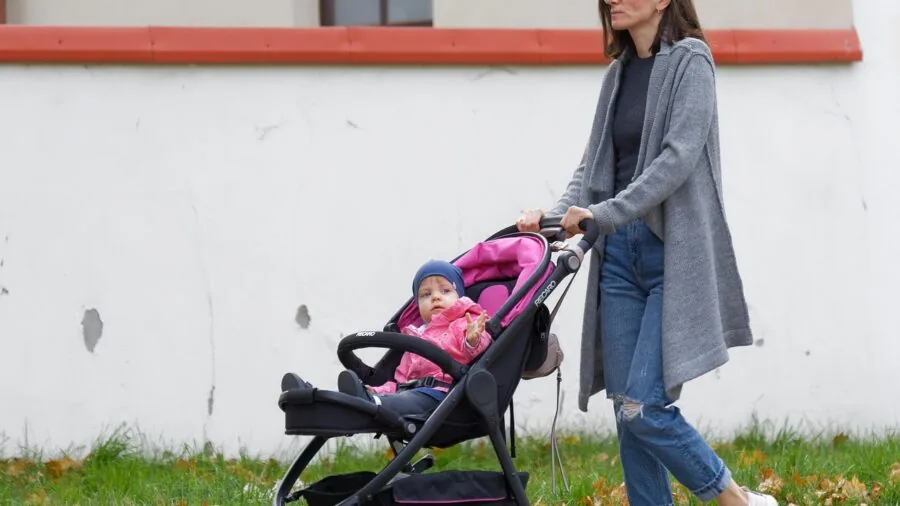 Parent pushing stroller on rainy street, baby visible through clear cover