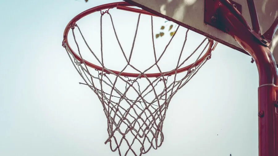 Parent struggling to assemble basketball hoop in driveway while child watches