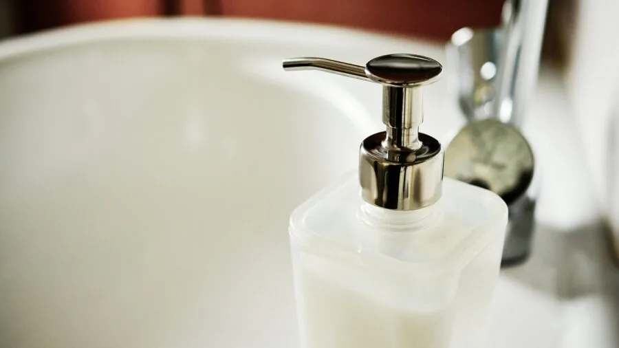Parent washing baby dishes and utensils in kitchen sink with warm water and soap