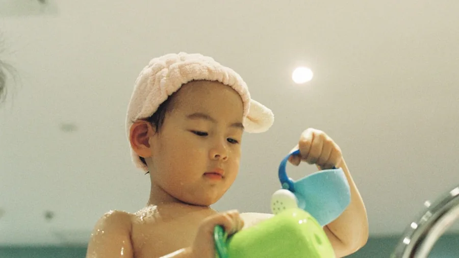 Parent washing infant toy under running water in kitchen sink