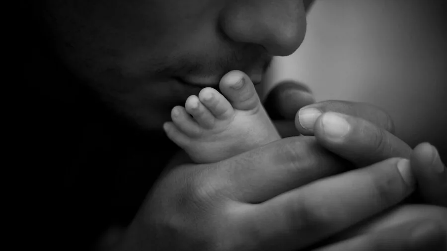 Parent's hands gently supporting baby during diaper change on padded surface