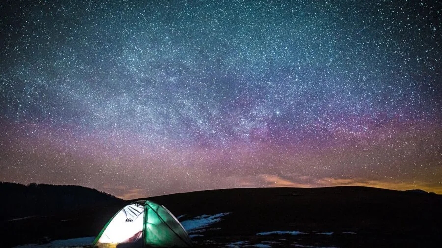 People gathered outside at night watching a movie under stars during a camping trip
