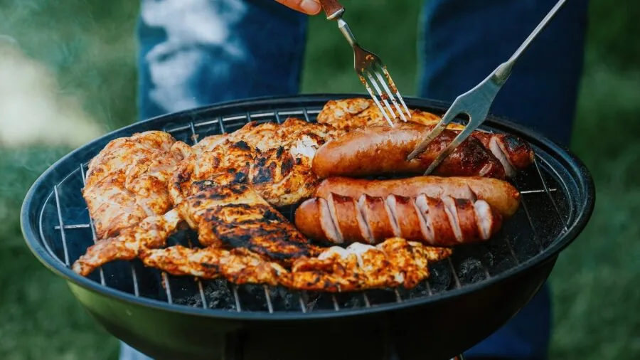 People gathering around an outdoor grill on a patio during an evening meal preparation